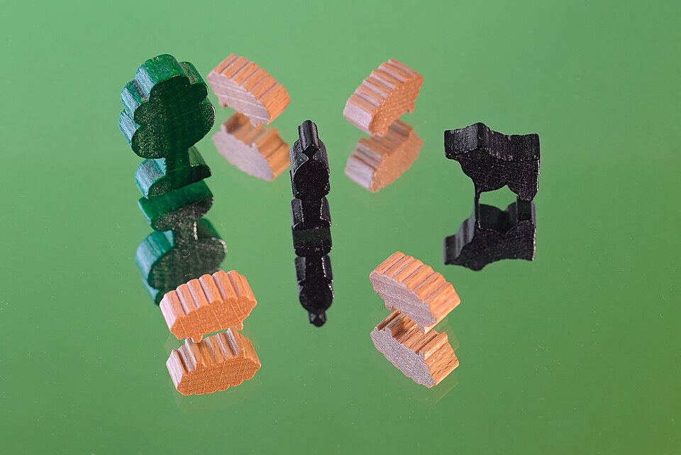 Small wooden toy figures of a shepherd, a flock of sheep, a dog, and a tree on a mirror